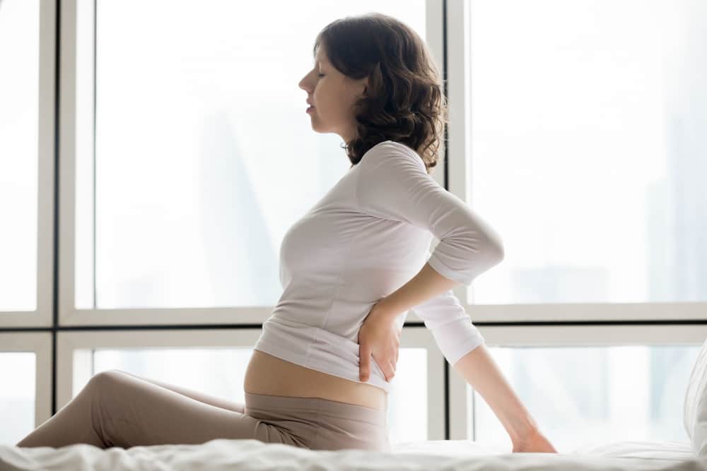 Pregnant woman holding her lower abdomen with anatomy illustration overlay